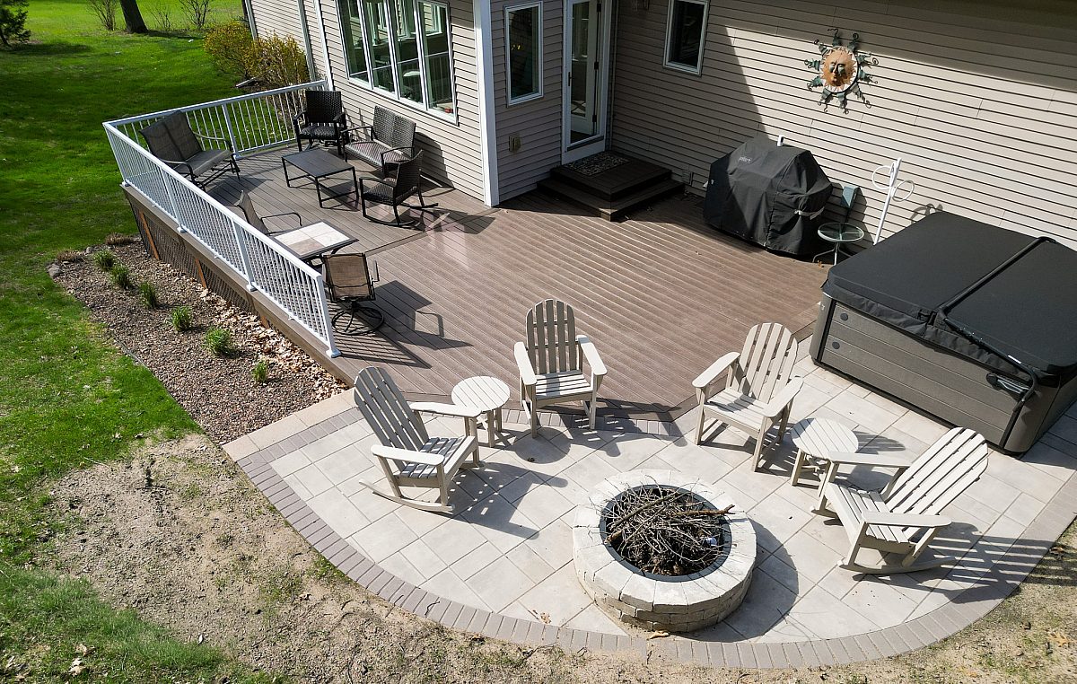 Paver patio with deck furniture and fire pit. Green Shield deck in Tropical Walnut color with white aluminum baluster deck railing visible in background of shot.