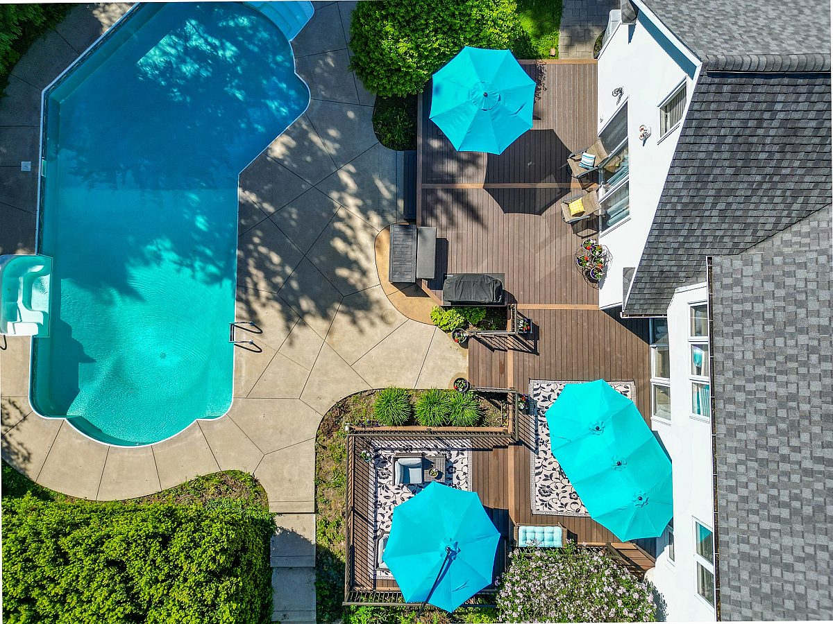 An aerial view captures the layout of this 751-square-foot Green Shield pool deck. Surrounded by greenery and patio furniture, the spacious structure is reliably engineered to support an expansive outdoor living area built to last.
