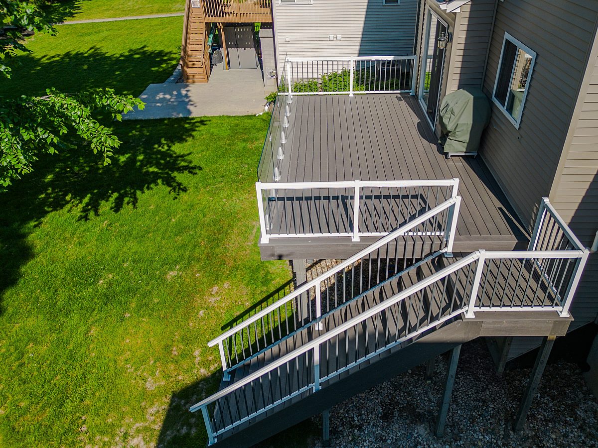 Side profile drone shot highlighting a full 13-step Ash Gray staircase and initial landing framed with white aluminum baluster railings. Green Shield pairs intentional upper-level layout space—like dedicated grill placement—with a foundation built to last.