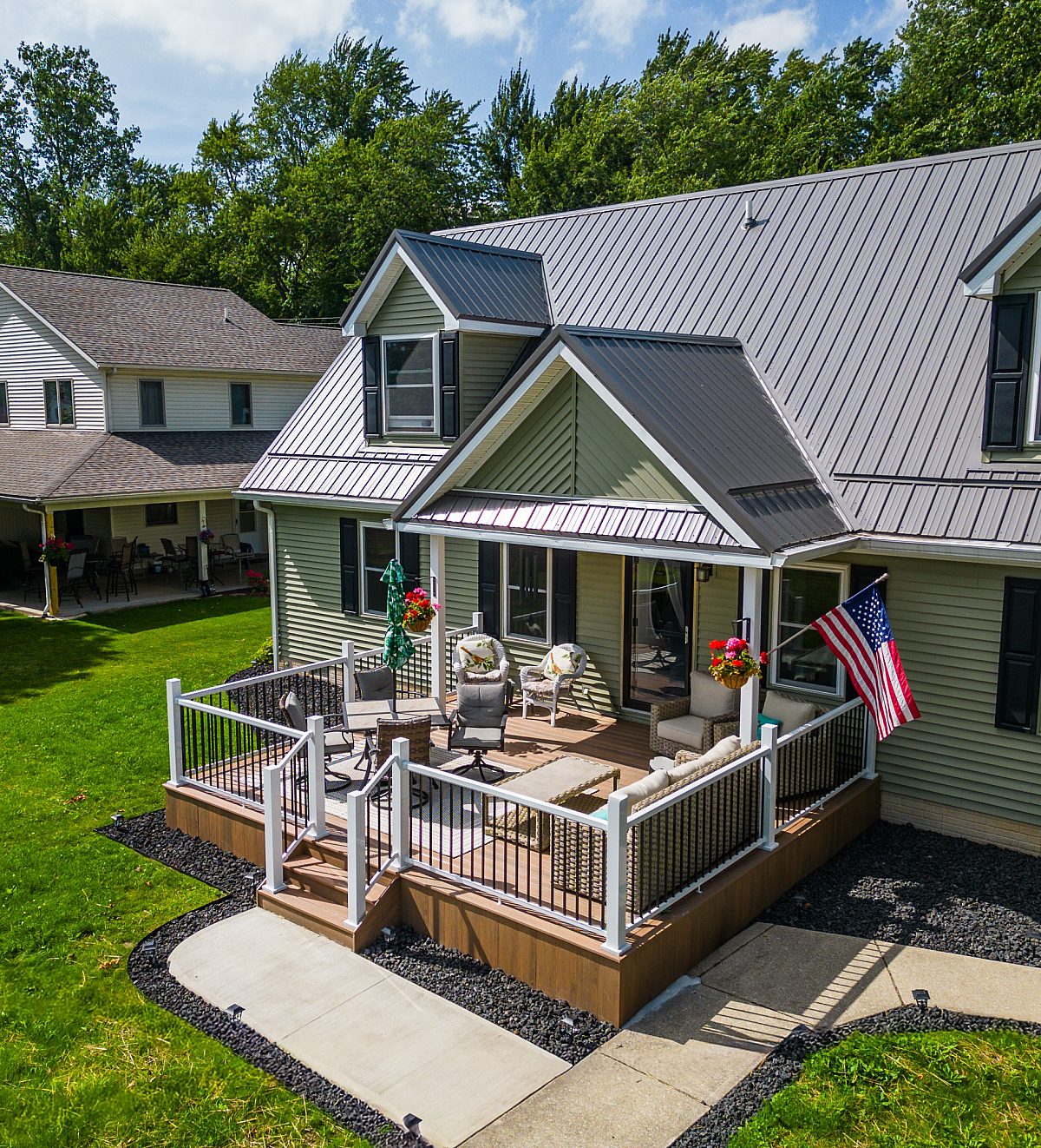 A manicured sidewalk leading to a fully-skirted Tigerwood front patio with seating and entertaining areas, black balusters with write railing, and two stairs built by America's #1 deck builder.