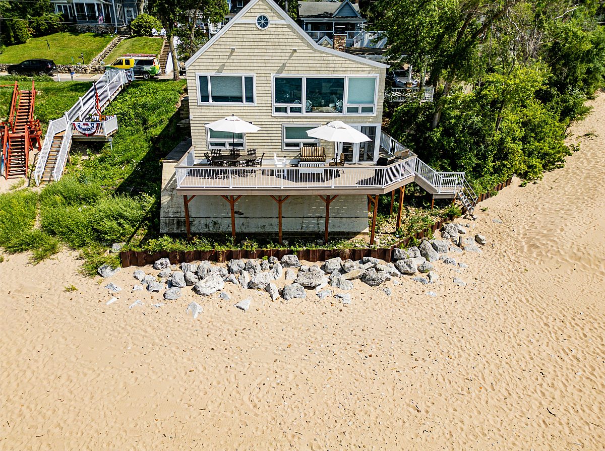 Green Shield Deck Builders' beach deck along beach front property with sand and rocks. Deck has furniture and white beach umbrellas for shade. Cream to tan colored home matched beautifully with Green Shield rice hull composite.