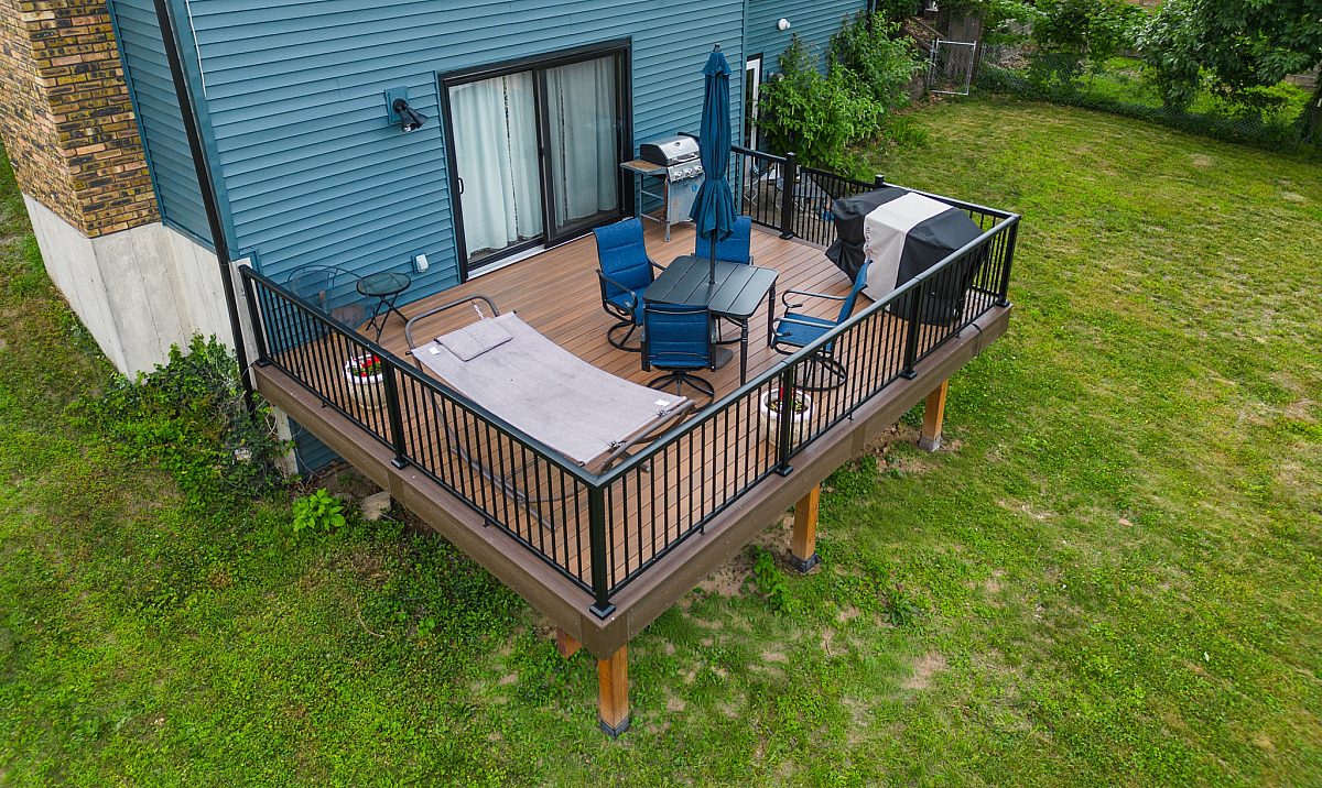 Tropical Walnut urban backyard deck with Tigerwood accents on a teal colored home. Features include Black Aluminum Baluster railings, a designated dining area, covered grill, and restful hammock.