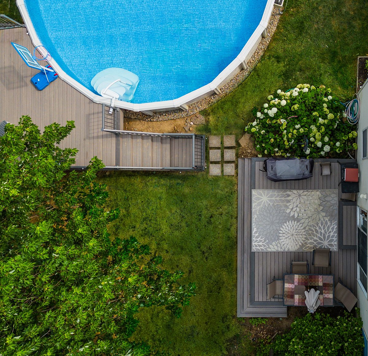 Multi-platform pool deck with Tigerwood decking and Tropical Walnut picture frame. Drone shot from above with pool basketball visible. Nice flowers and tree along side of deck.