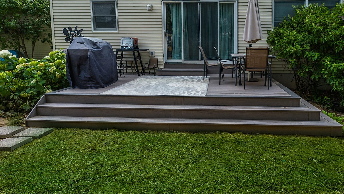 Railing-free deck with cascading stairs, featuring a covered grill and cook area, as well as a dining area with umbrella.